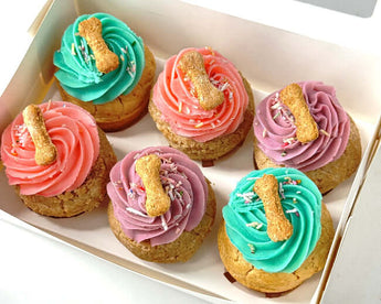 A delicious box of dog-friendly pupcakes topped with colorful icing and dog biscuits, perfect for a dog party.